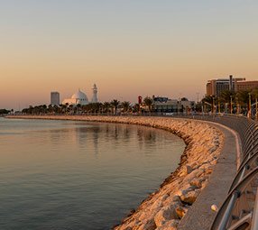 A serene waterfront promenade with a mosque and city skyline at sunset | MSC Cruises
