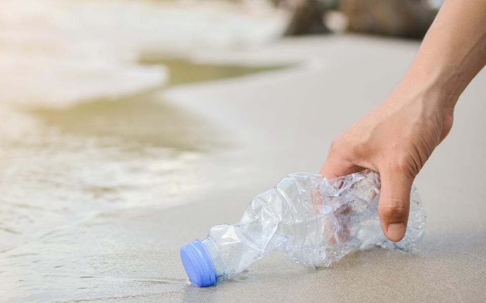 A hand picking up a plastic bottle from the beach to promote sustainability | MSC Cruises A hand picking up a plastic bottle from the beach to promote sustainability | MSC Cruises