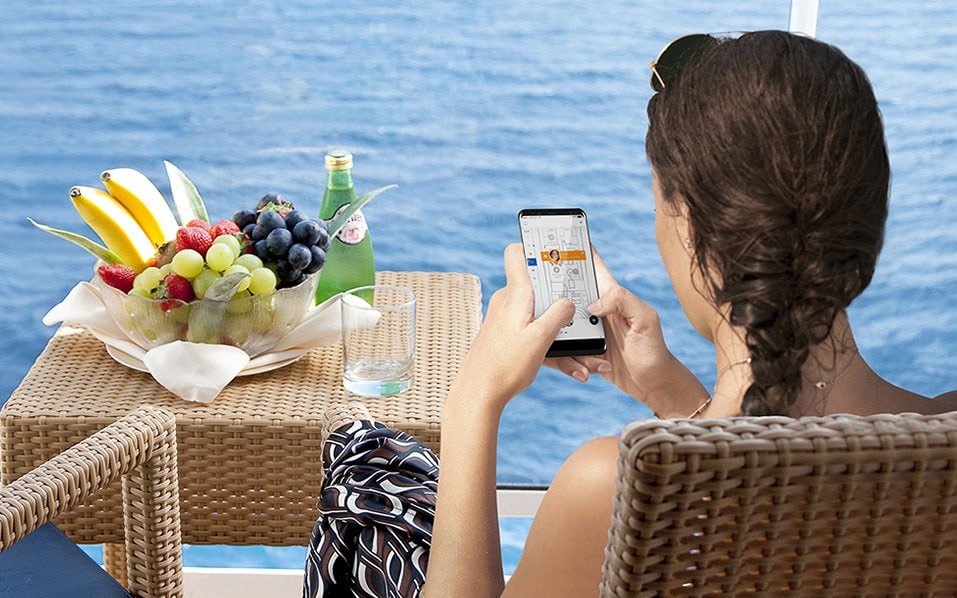 Woman relaxing on a balcony with ocean view, using a smartphone, next to fresh fruit and sparkling water | MSC Cruises Woman relaxing on a balcony with ocean view, using a smartphone, next to fresh fruit and sparkling water | MSC Cruises