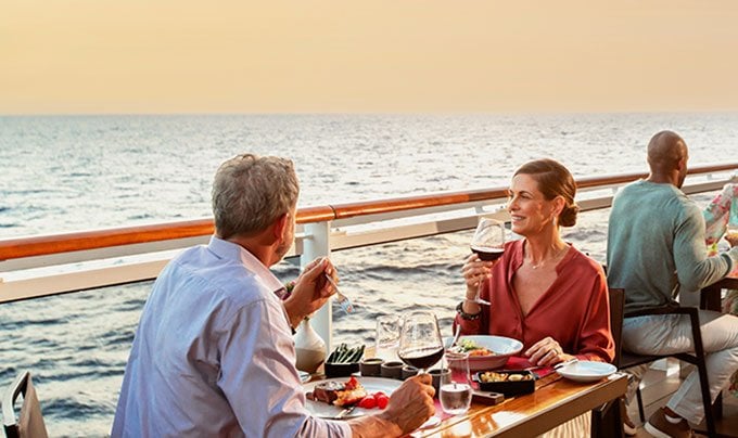 Couple dining on a cruise ship deck overlooking the ocean at sunset | MSC Cruises Couple dining on a cruise ship deck overlooking the ocean at sunset | MSC Cruises