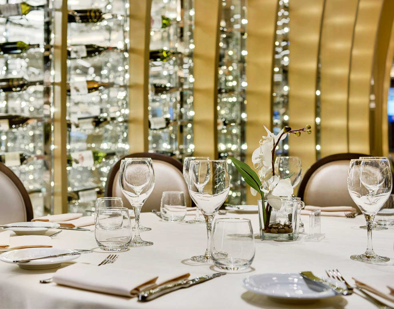 Elegant dining table with wine glasses and orchid centerpiece in a luxurious cruise setting | MSC Cruises Elegant dining table with wine glasses and orchid centerpiece in a luxurious cruise setting | MSC Cruises
