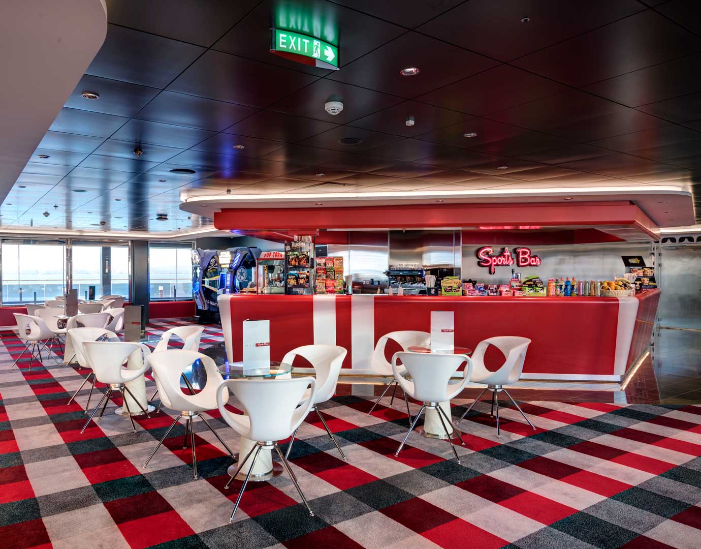 Modern sports bar with red decor, white chairs, and snack options onboard a cruise ship | MSC Cruises Modern sports bar with red decor, white chairs, and snack options onboard a cruise ship | MSC Cruises