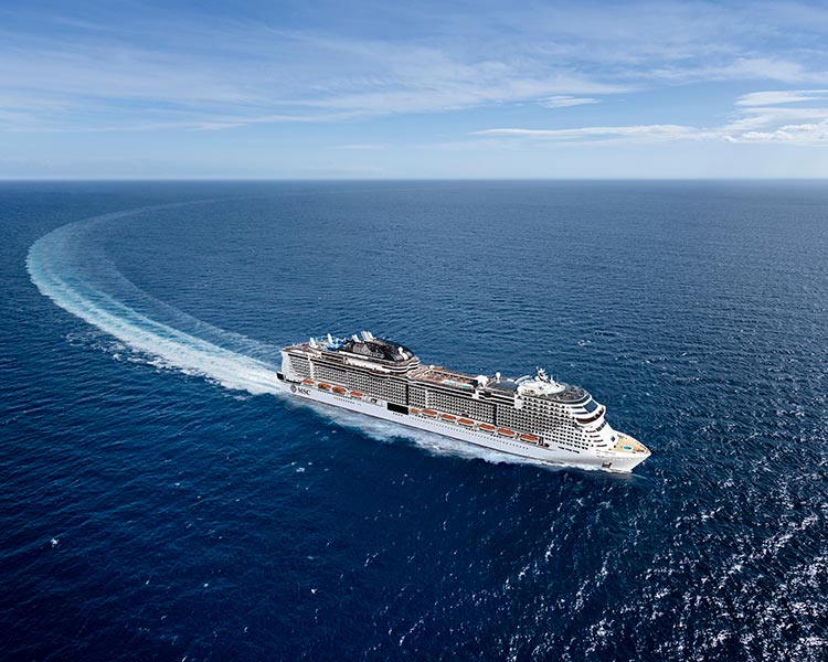 An MSC cruise ship making a wide turn on open blue waters under a clear sky | MSC Cruises An MSC cruise ship making a wide turn on open blue waters under a clear sky | MSC Cruises